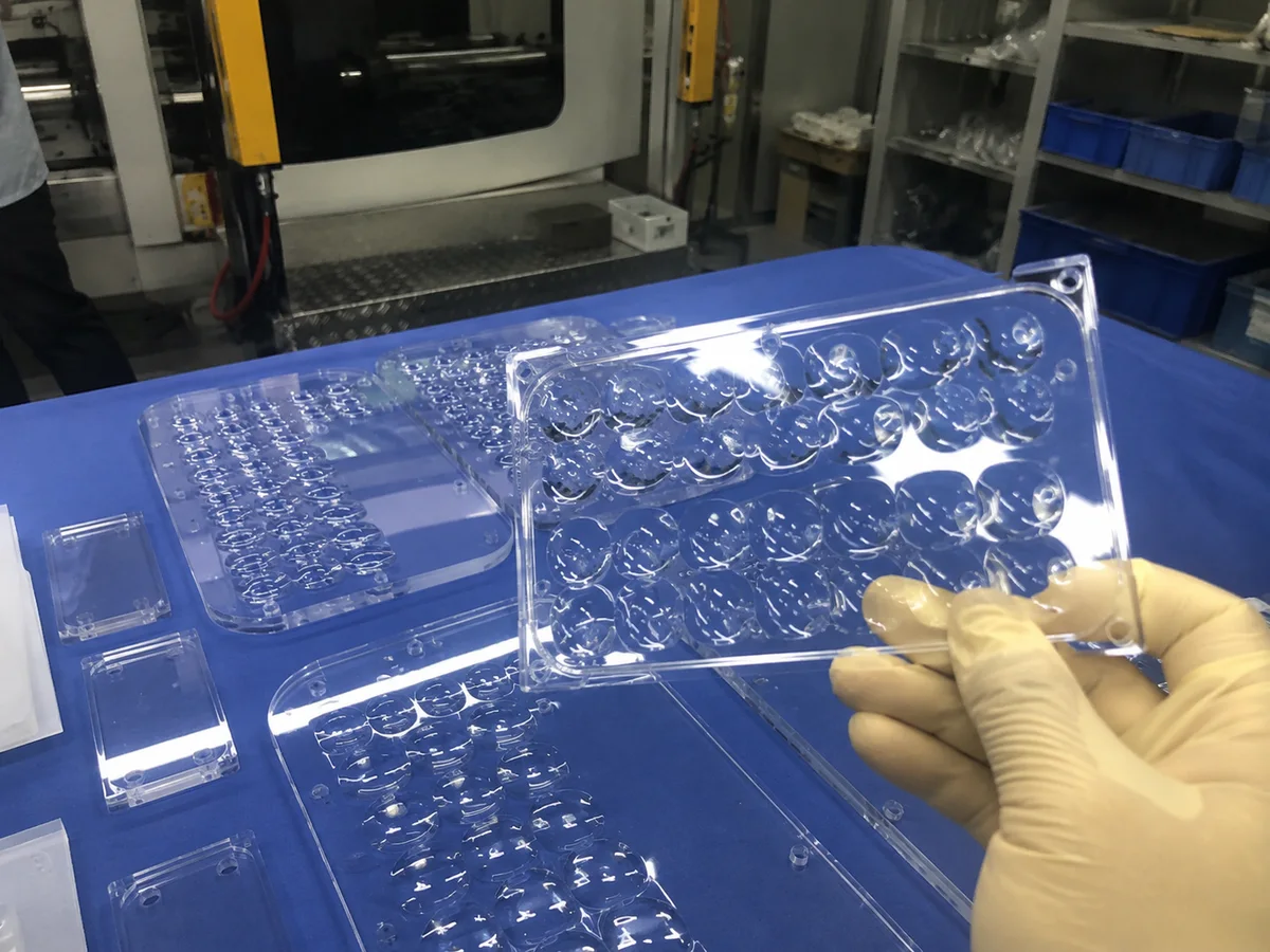 Clear acrylic optical cover checked by hand on a shop floor bench